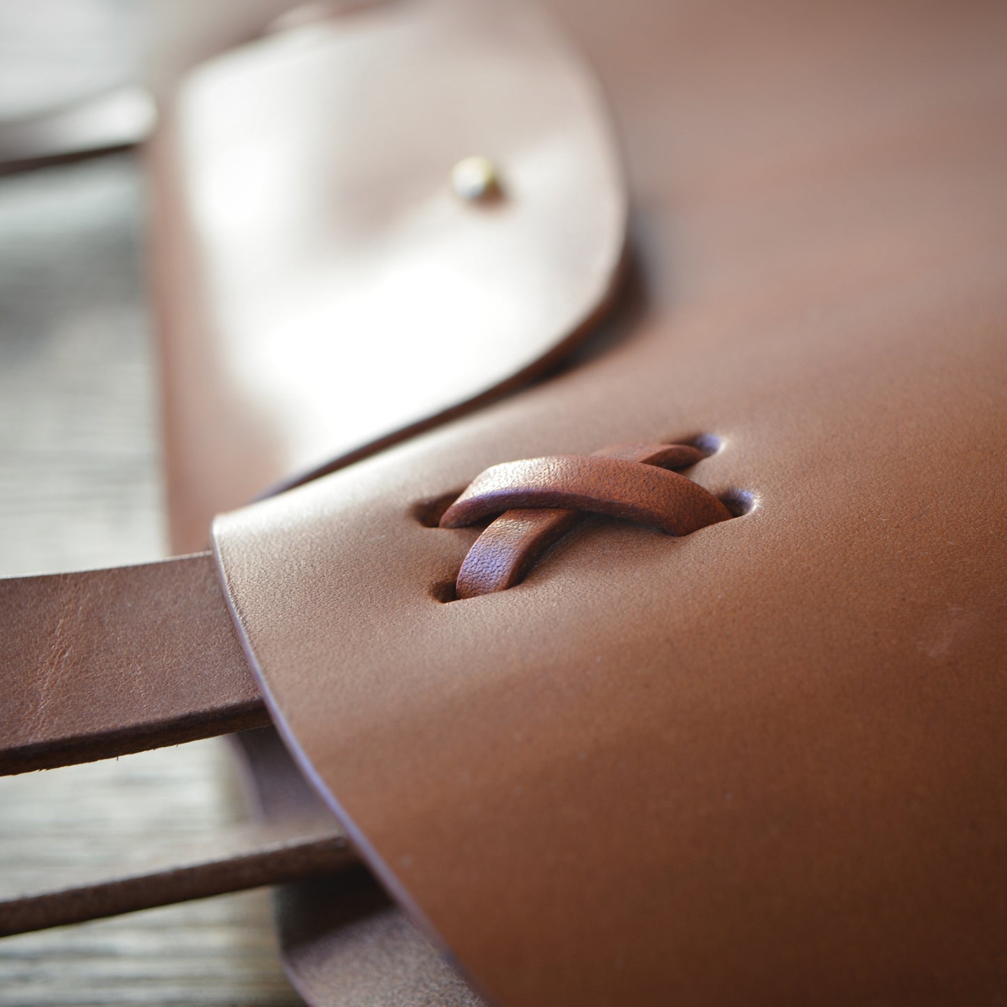 Close up of criss cross lacing strap attachment on caramel color leather bag.