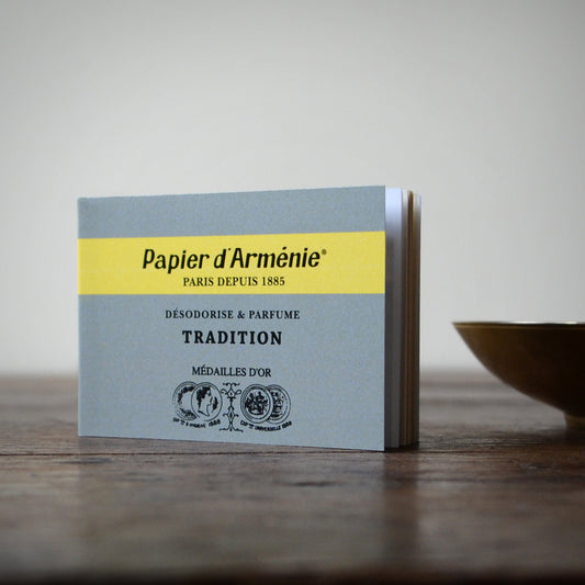 A booklet of traditional Papier d'Armenie standing on  wood surface with a brass bowl to the side.
