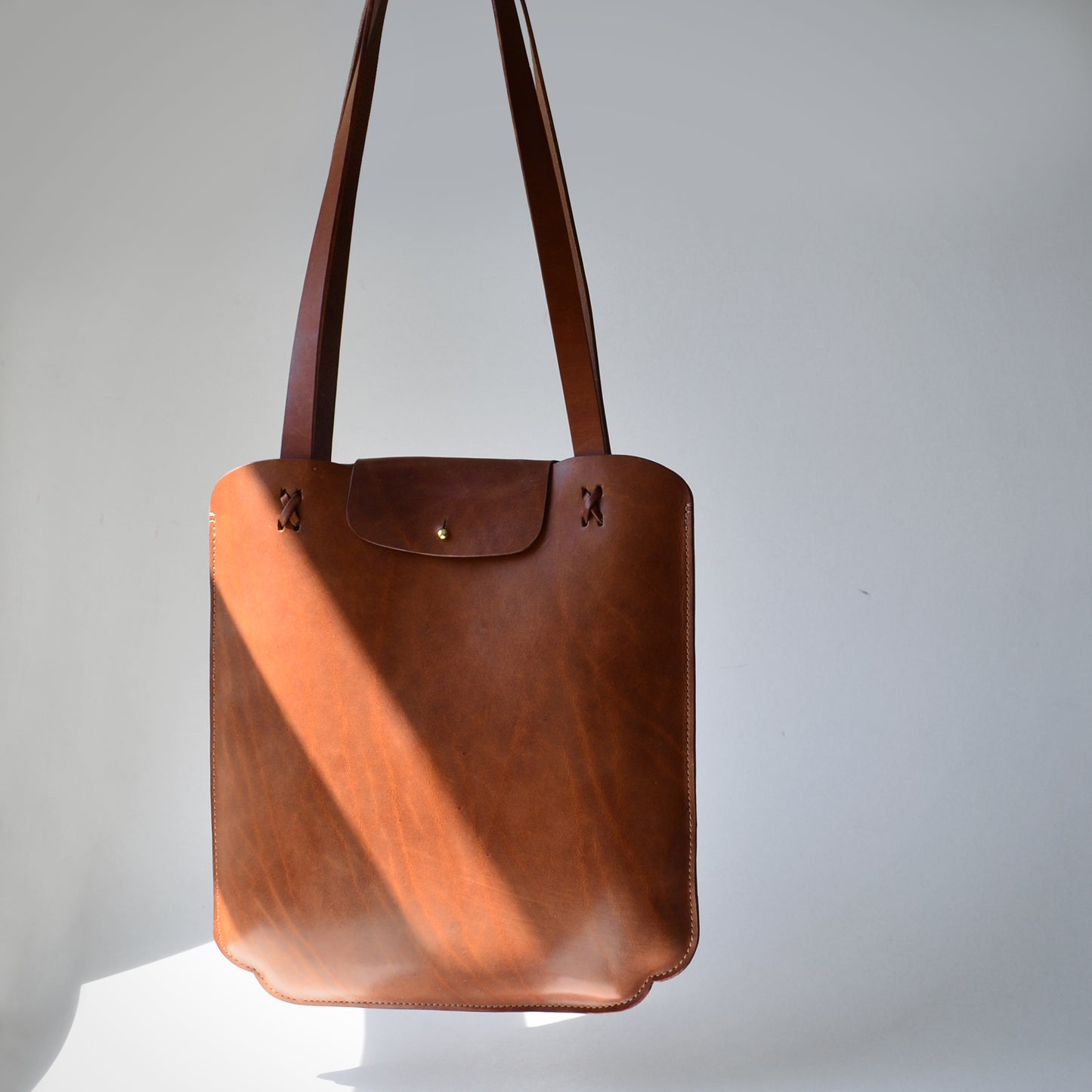 Scalloped Slim tote bag product image. Caramel color leather bag in sunlight stream.